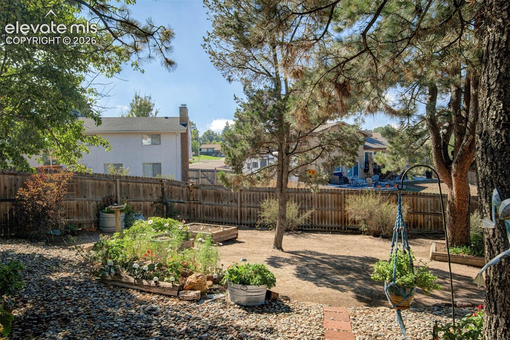 Expansive backyard featuring mature trees, raised garden beds, a fenced perimeter, and flagstone pavers