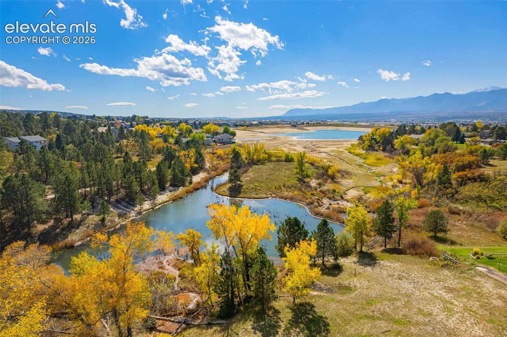 Aerial perspective featuring a natural pond, dense mature foliage, open terrain, and distant mountain topography