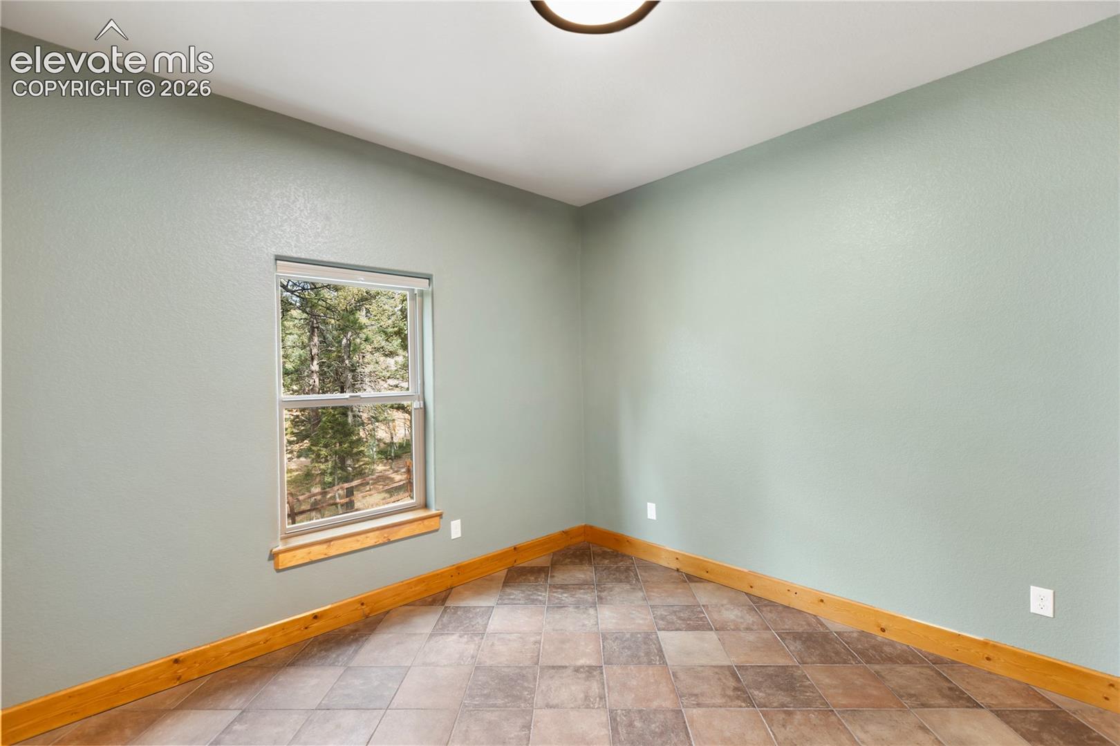Neutral-toned interior space featuring light green walls, a single-hung window with a wood-finish sill, natural wood trim, and tile flooring