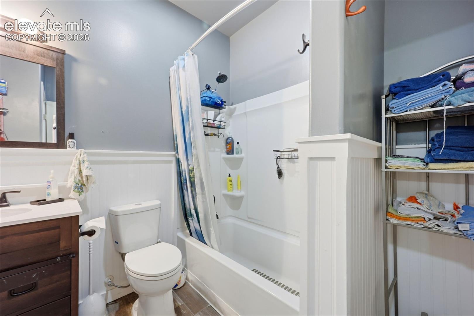 Bathroom featuring a white tub/shower combination, dark wood-finish vanity with a white countertop, and wainscoting