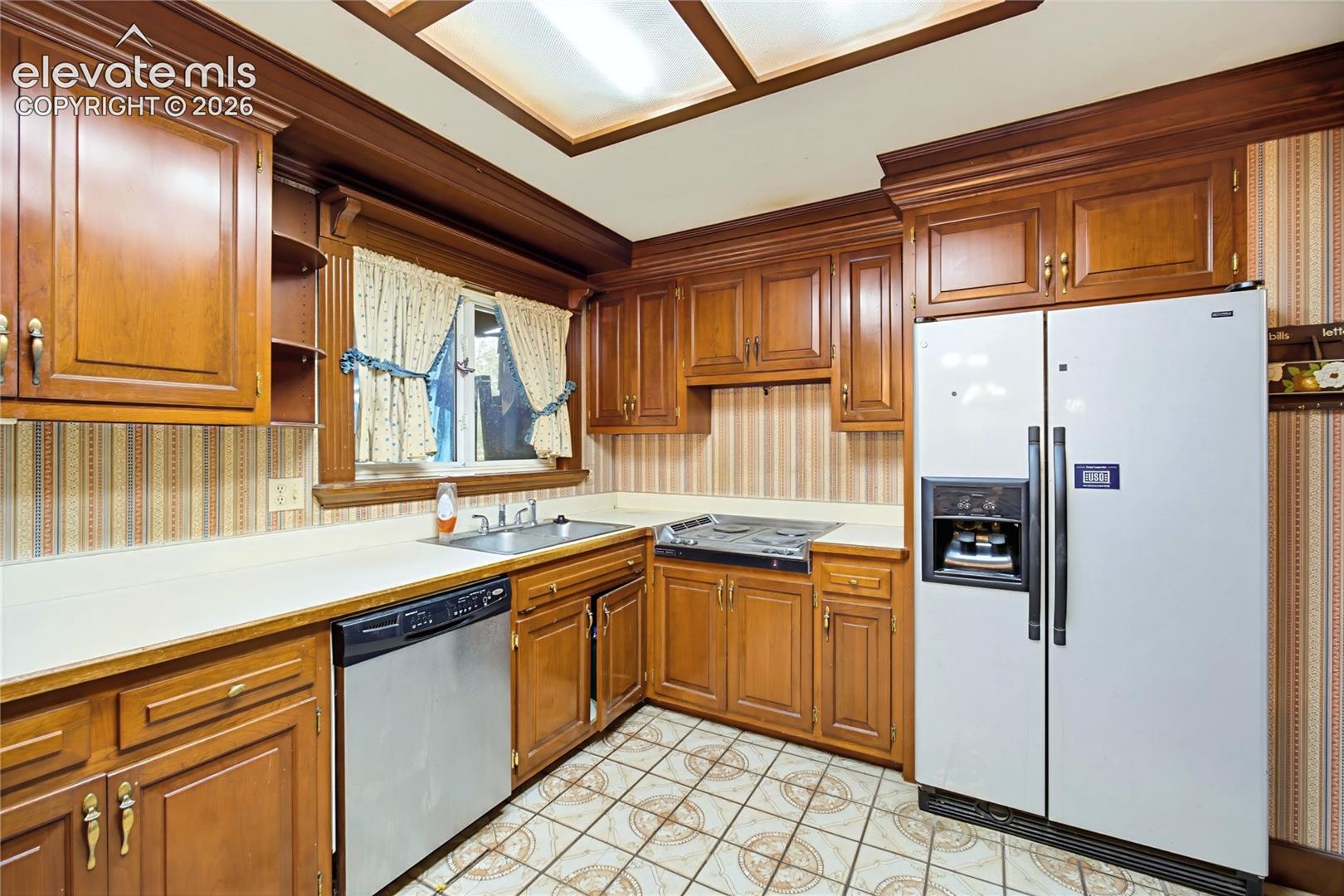 Kitchen featuring wood cabinetry, light-toned countertops, a stainless steel dishwasher, and a side-by-side refrigerator
