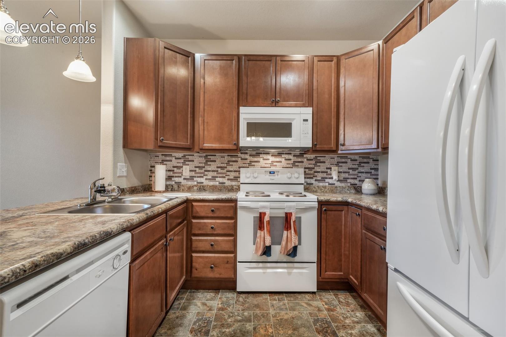 Kitchen featuring wood-finish cabinetry, white appliances, a mosaic tile backsplash, and a double basin sink