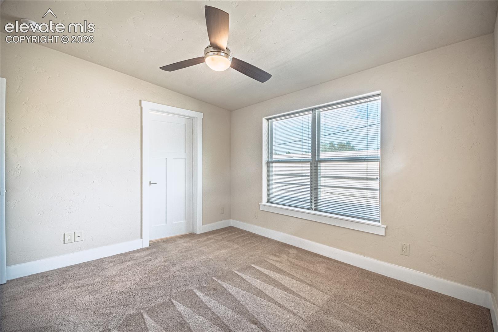 Carpeted interior space featuring a ceiling fan with integrated lighting, a multi-panel interior door, and a window with blinds