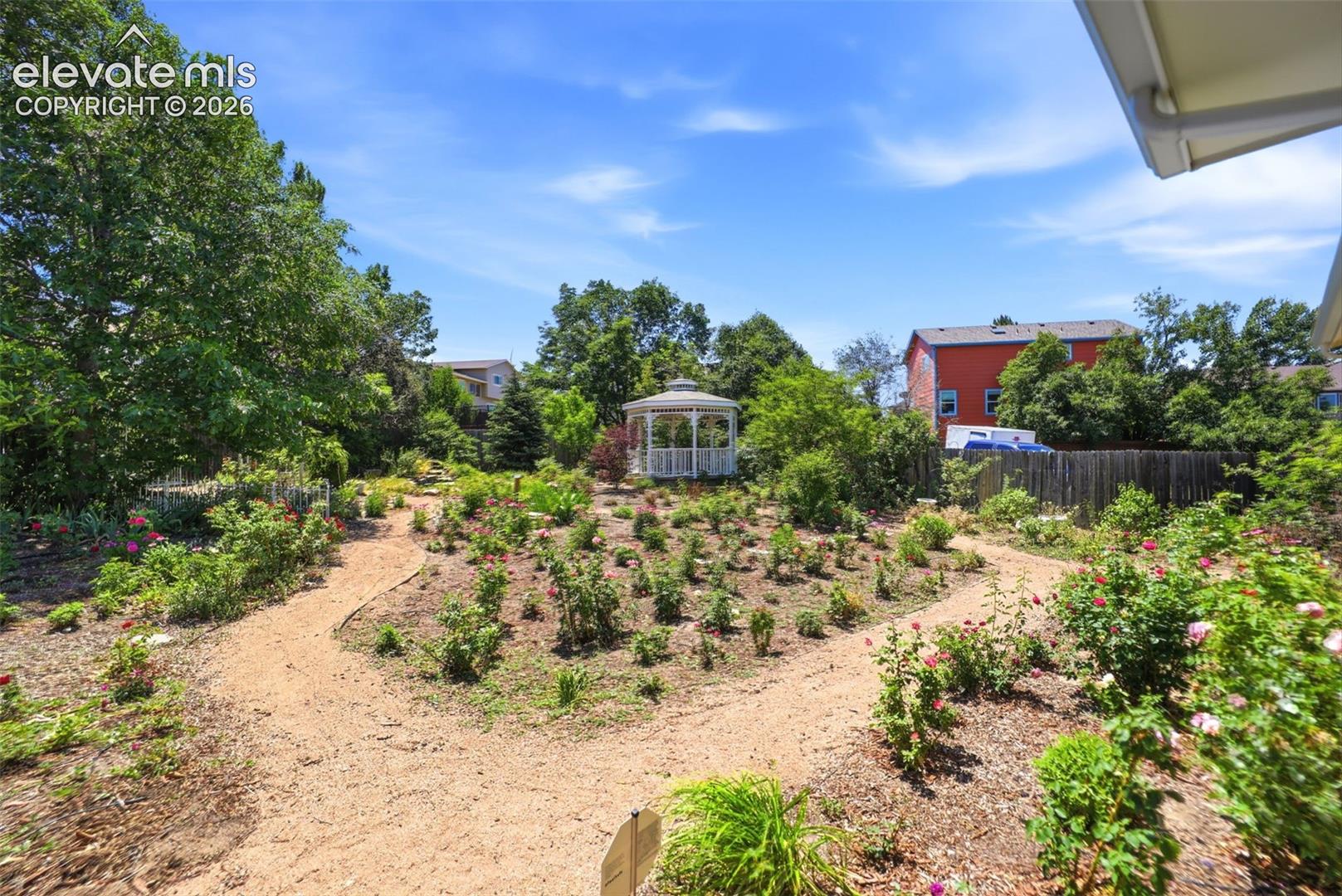 Landscaped garden featuring a central white gazebo, multiple walking paths, established plantings, and mature perimeter trees
