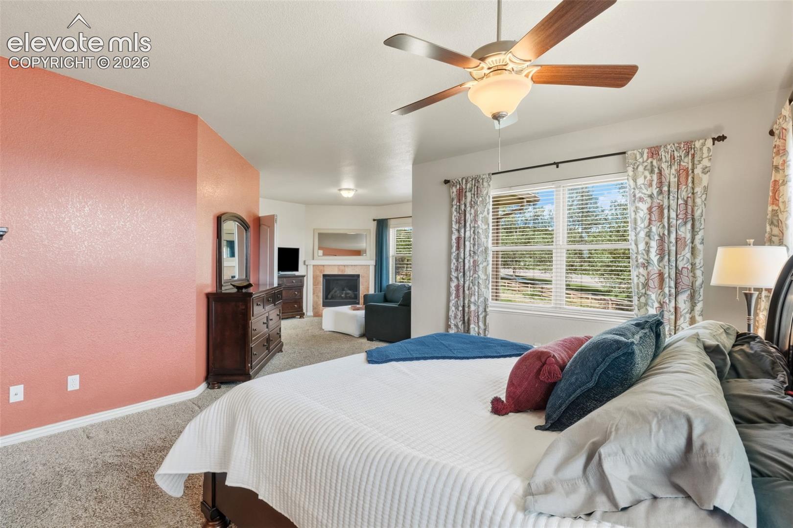 Recessed ceiling fan with wood-finish blades, window with blinds and floral pattern drapes, and a fireplace with a light-colored stone surround