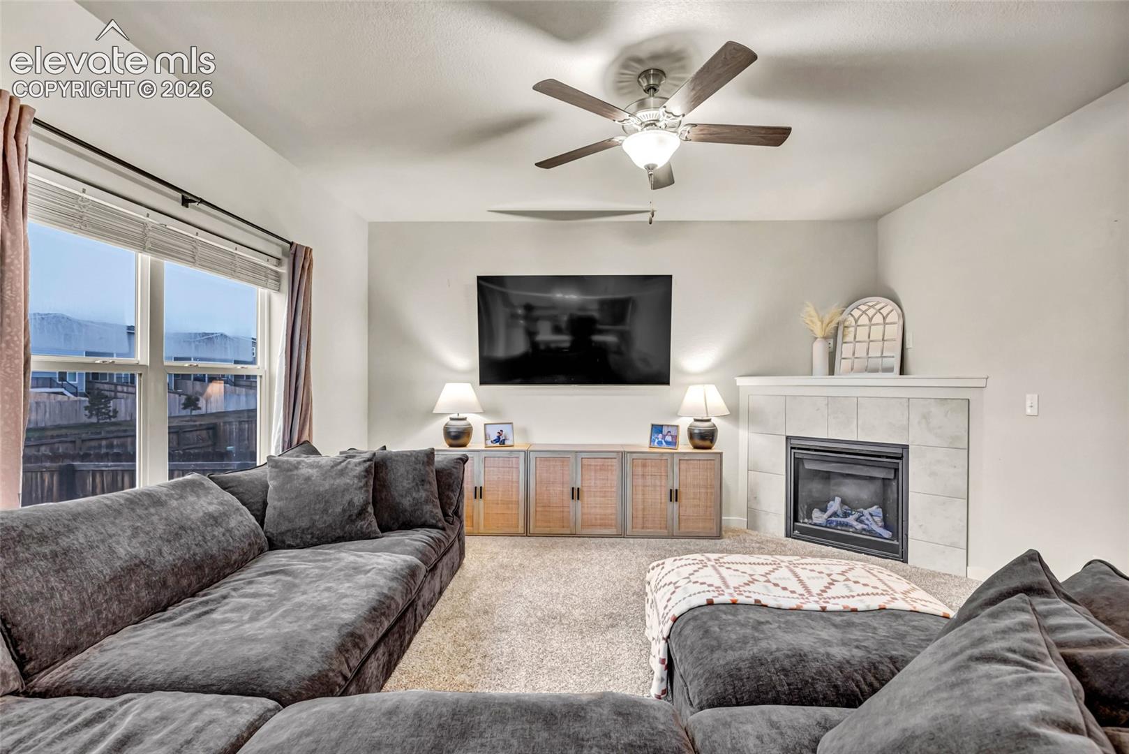 Recessed lighting, ceiling fan with integrated light, tiled fireplace with mantel, window with blinds, and carpeting