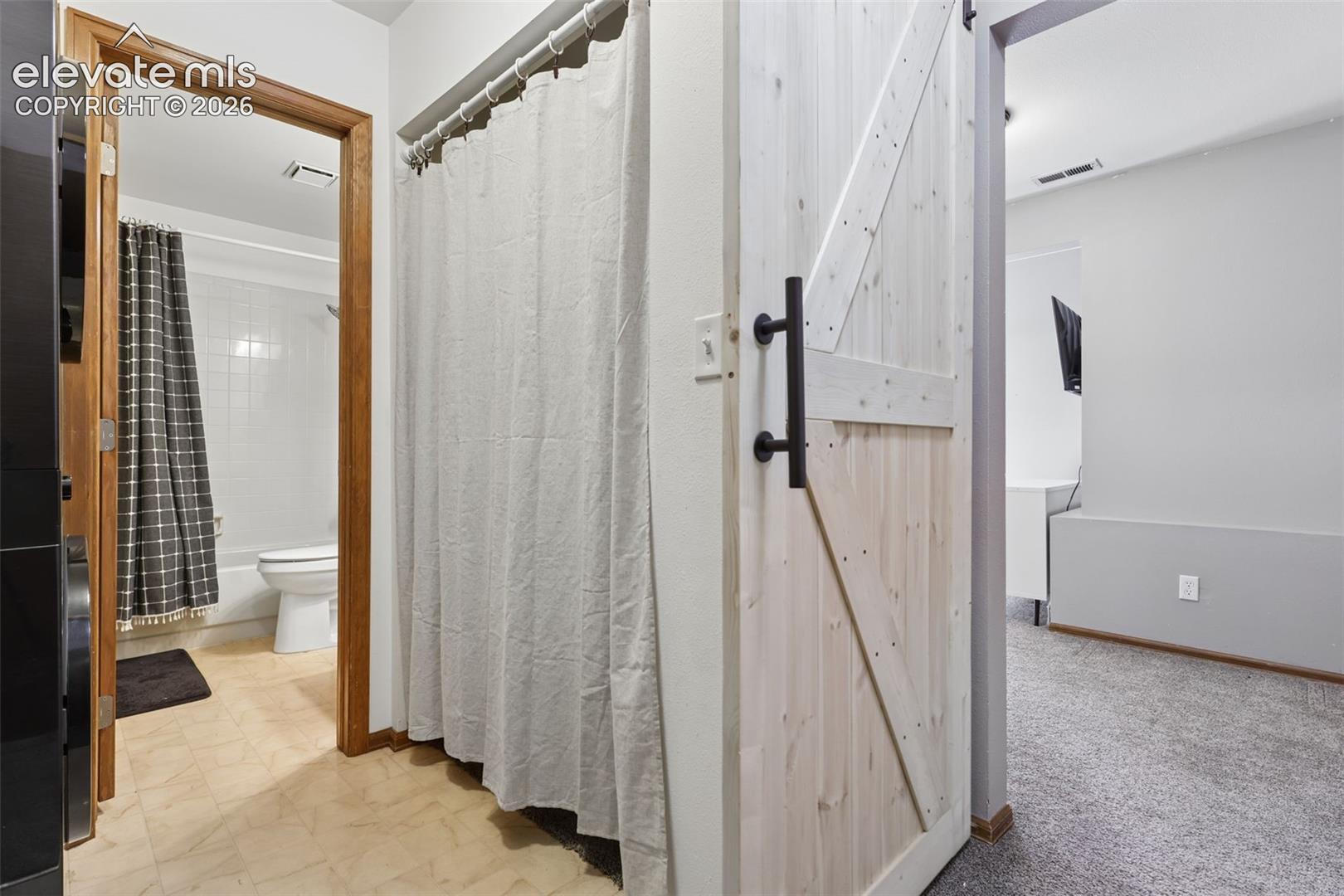 Light wood-finish barn door with black hardware, white walls, and gray carpeting