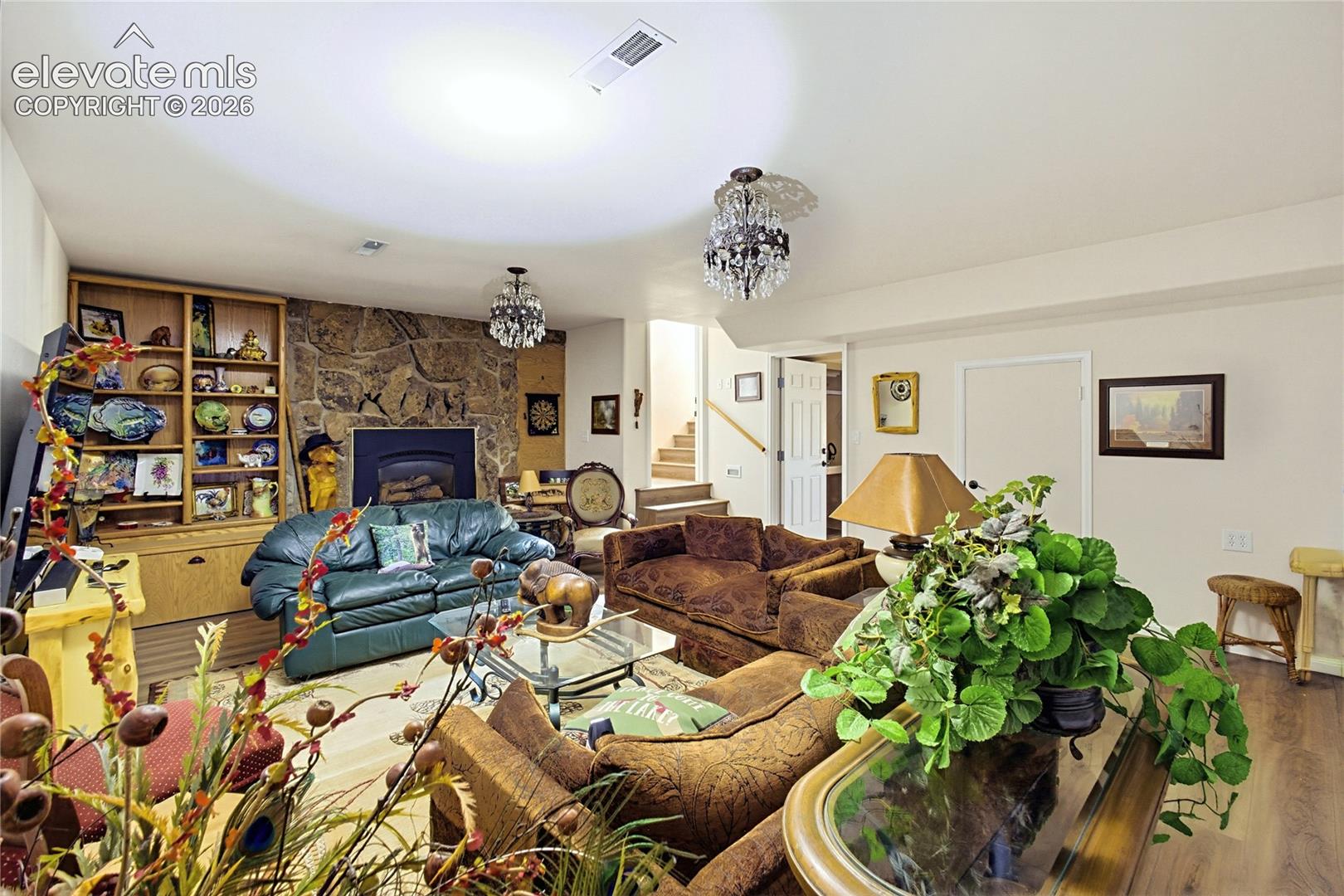 Living area featuring a floor-to-ceiling natural stone fireplace, built-in wooden cabinetry, crystal-accented chandeliers, and wood-finish flooring
