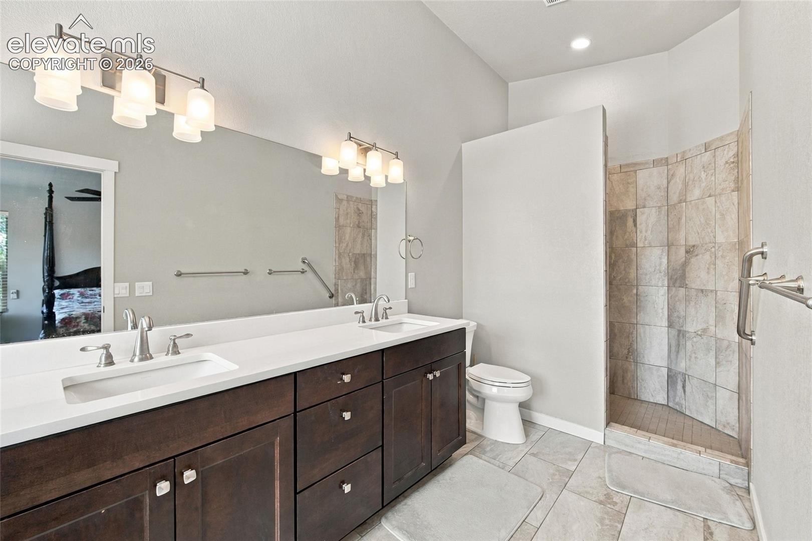 Dual-sink vanity with dark-finish cabinetry, countertop with integrated basins, full-width vanity mirrors, and a walk-in tiled shower