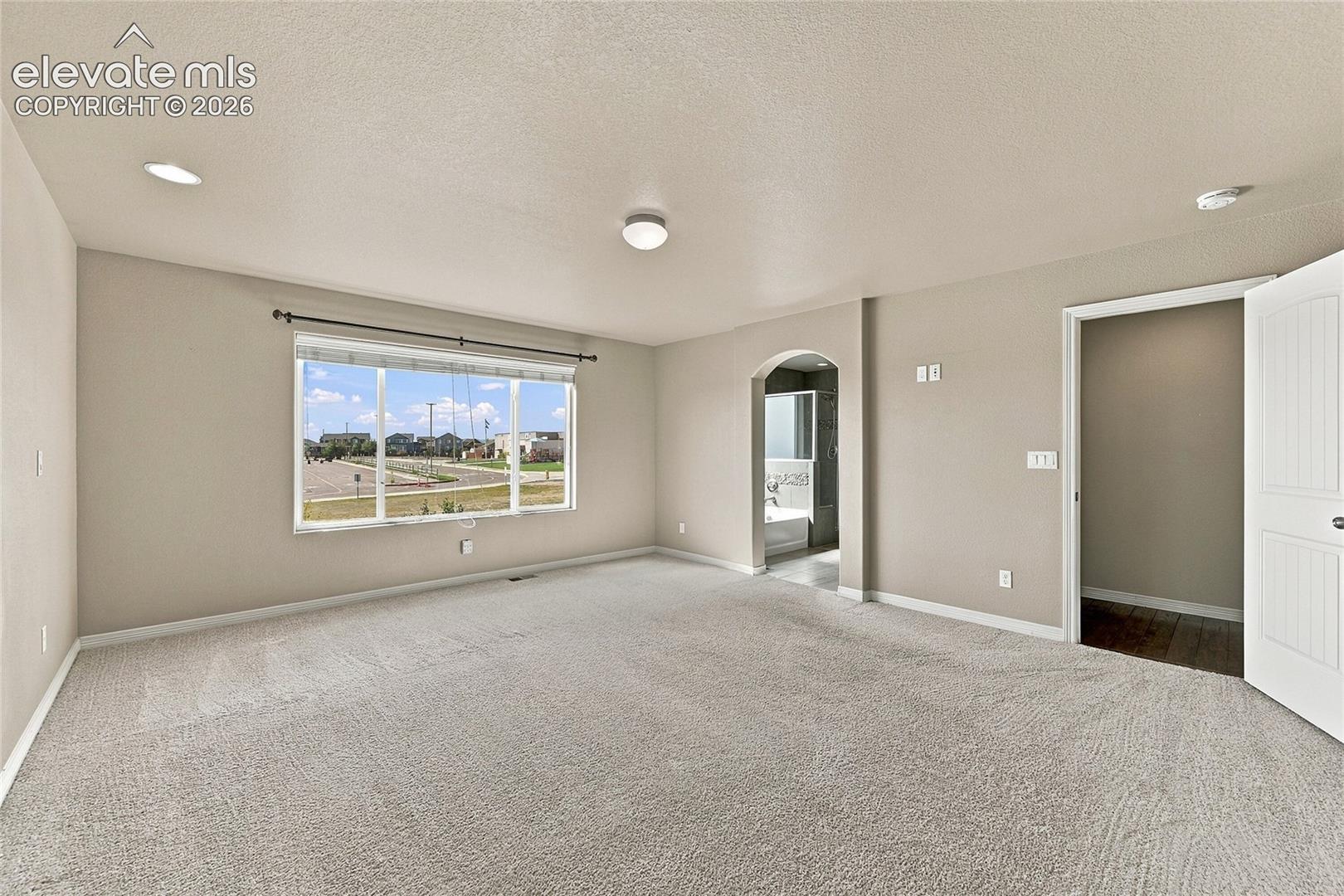 Room featuring neutral carpeting, recessed lighting, an expansive window with natural light, and an arched doorway