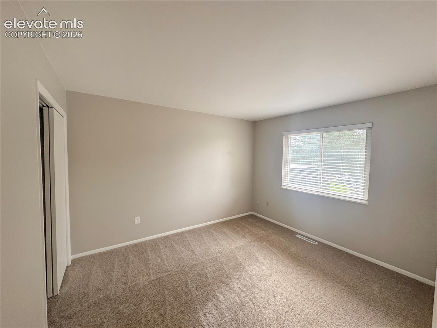 Neutral-toned walls, wall-to-wall carpeting, and a dual-pane window with fitted blinds