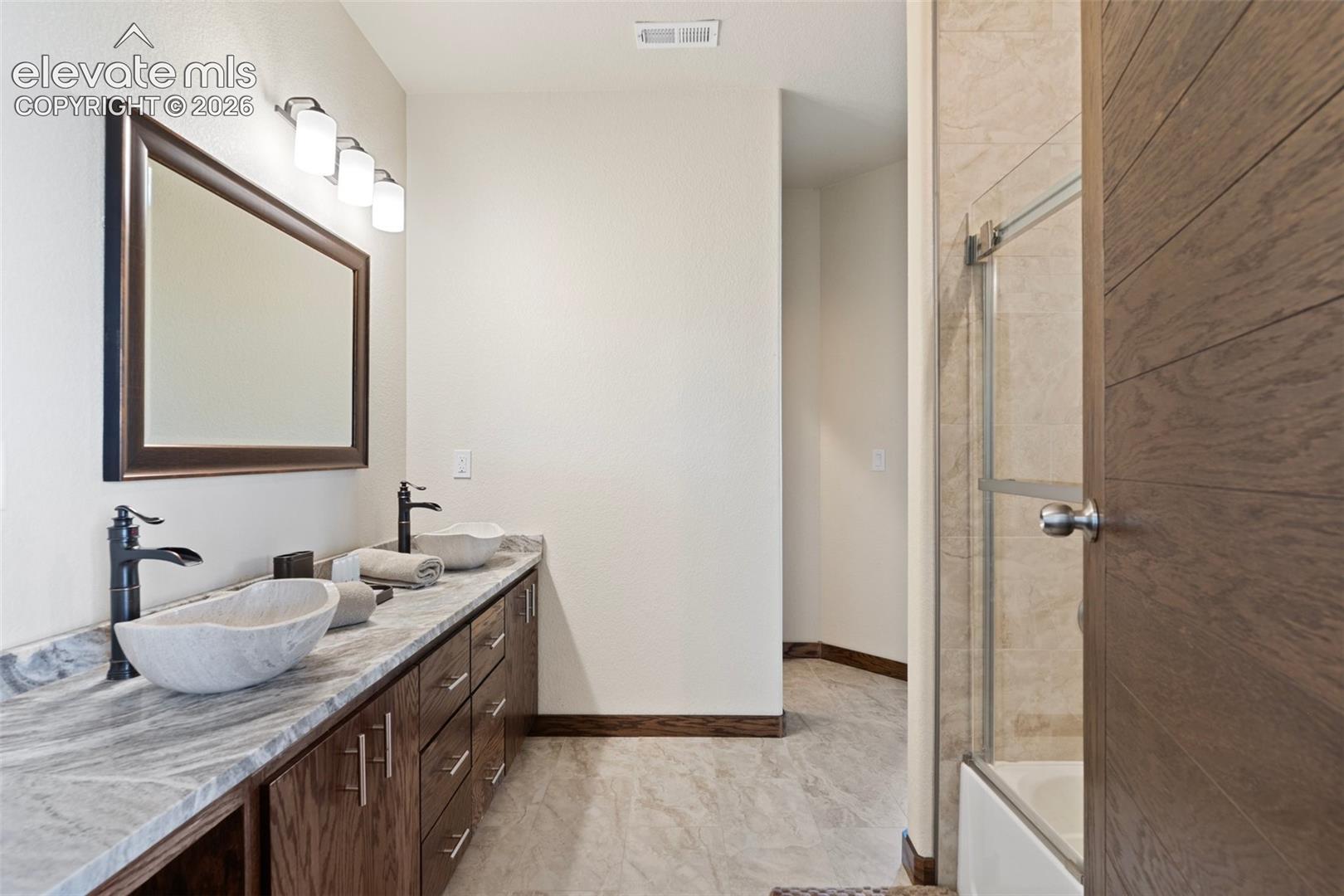 Jack and Jill bath with dual vessel sinks, matte black fixtures set atop a stone-finish countertop, complementing the dark wood-finish cabinetry