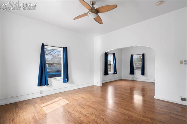 Empty room featuring a ceiling fan, wood finished floors, arched walkways, and plenty of natural light