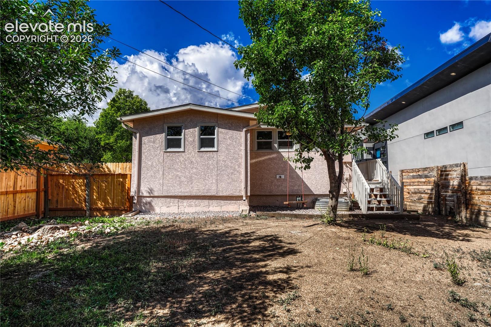 Expansive backyard featuring a new wood fence, mature trees, and an exterior staircase