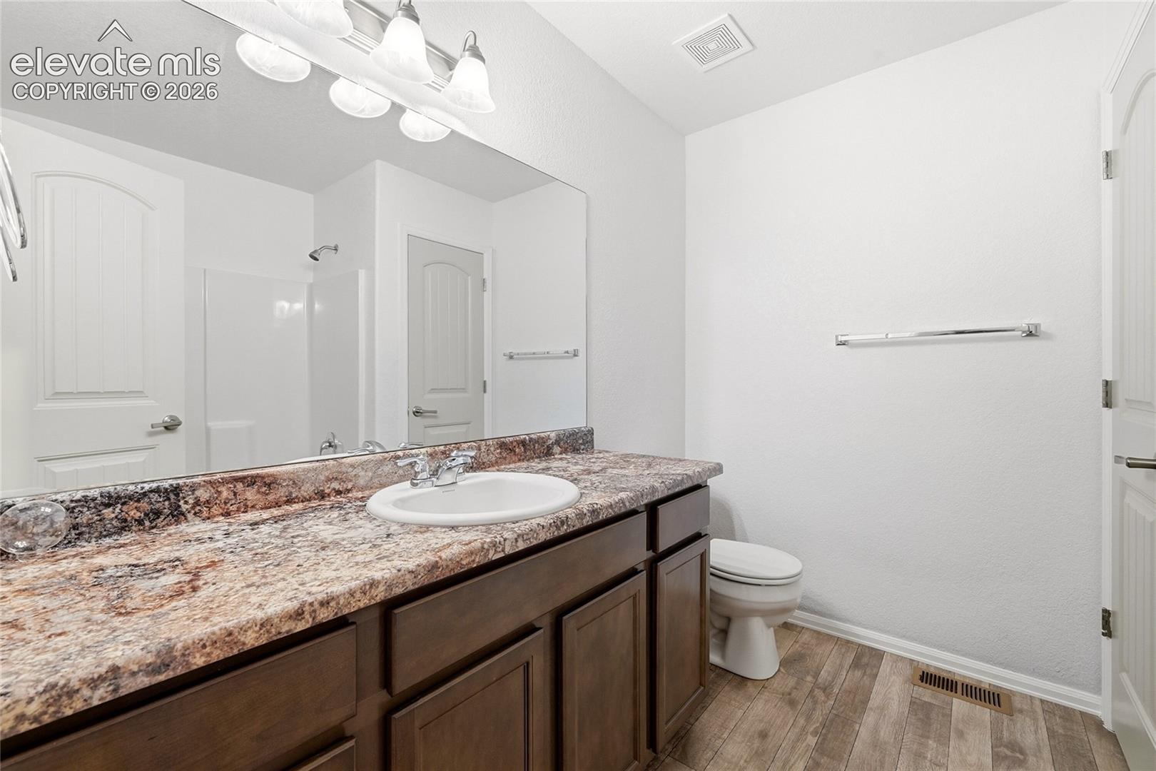 Bathroom featuring a vanity with a stone-finish countertop, undermount sink, multi-light fixture, full-width mirror, and wood-finish flooring
