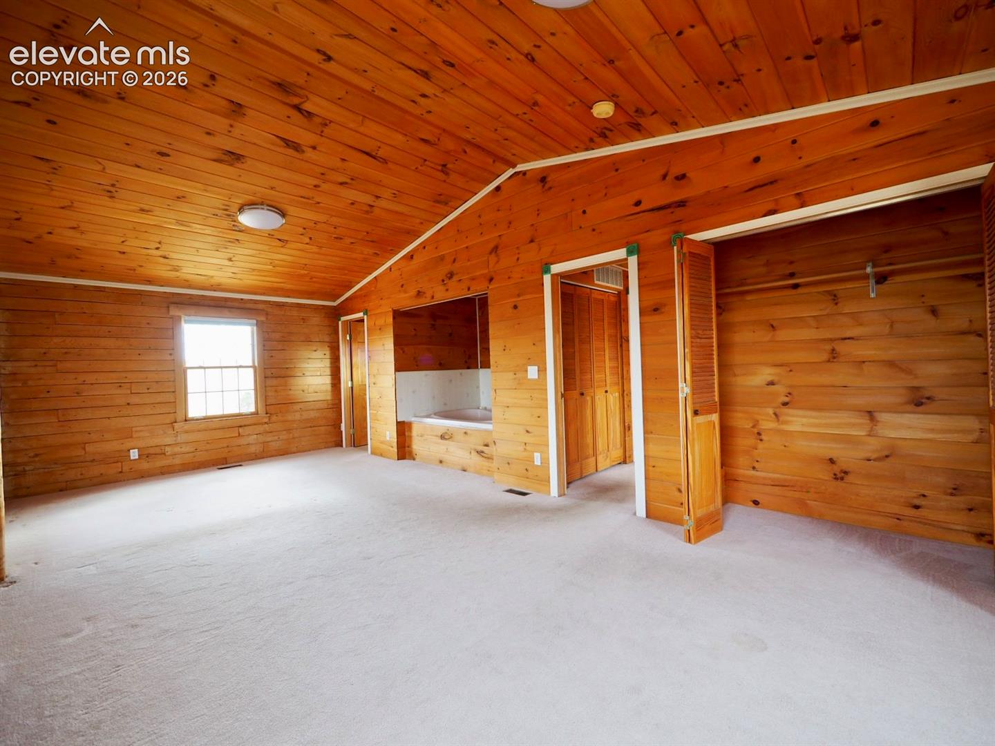 Vaulted wood-paneled ceiling, knotty wood-plank walls, integrated soaking tub alcove, and built-in closet with louvered doors