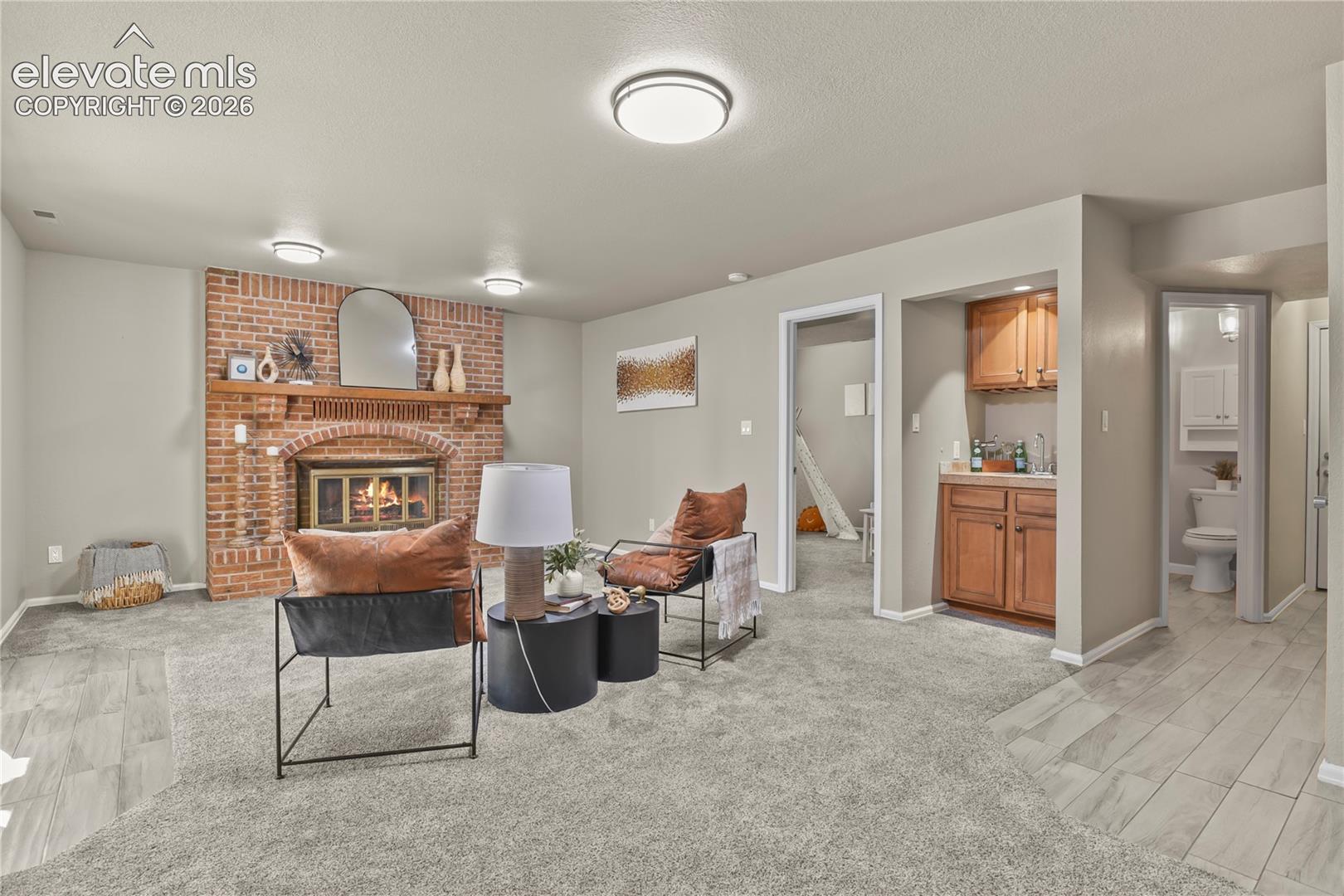 Living area featuring a floor-to-ceiling brick fireplace with a wood mantel, built-in wet bar with cabinetry, flush-mount ceiling lighting, and neutral carpeting