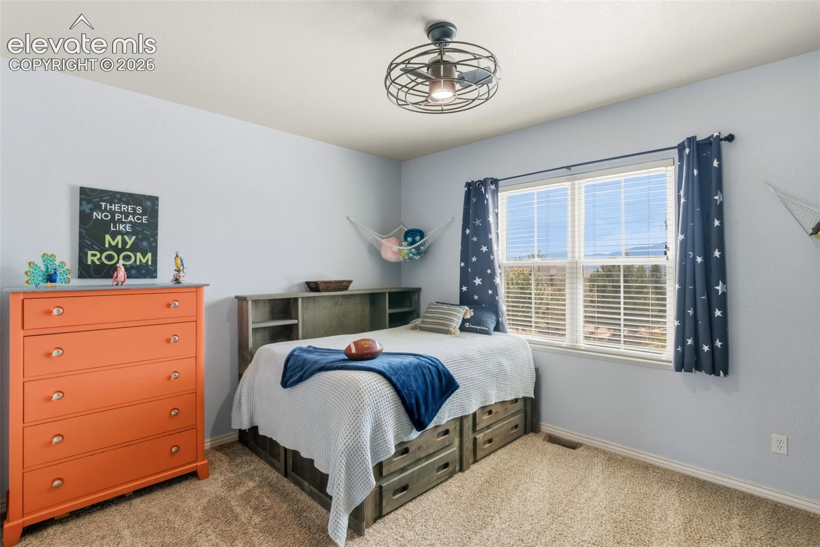 Spacious room featuring a large window, carpet flooring, a ceiling fan with integrated lighting, and a built-in bed frame with storage drawers