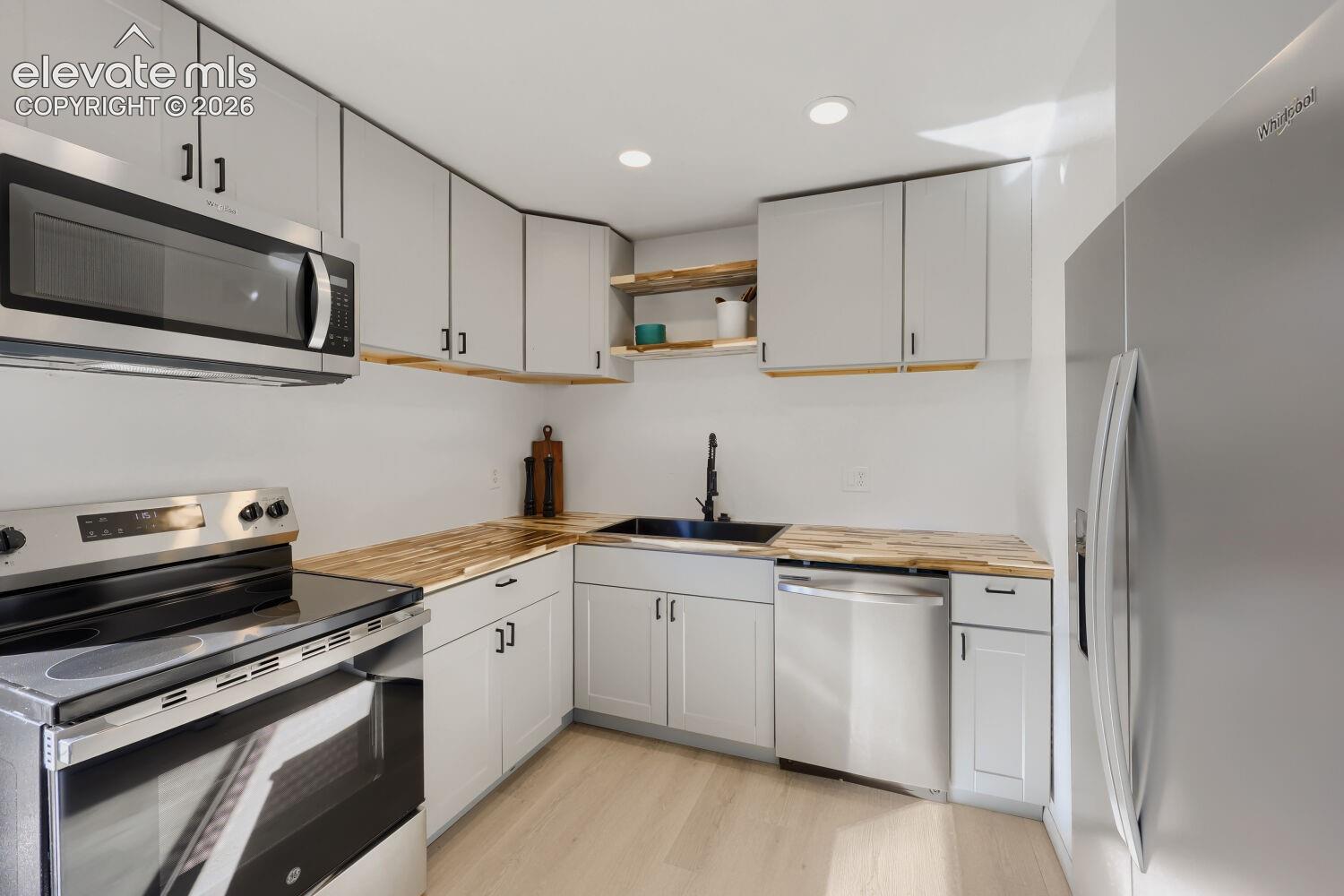 Stainless steel appliances, light gray cabinetry, wood-finish countertops, black sink, and light wood-finish flooring