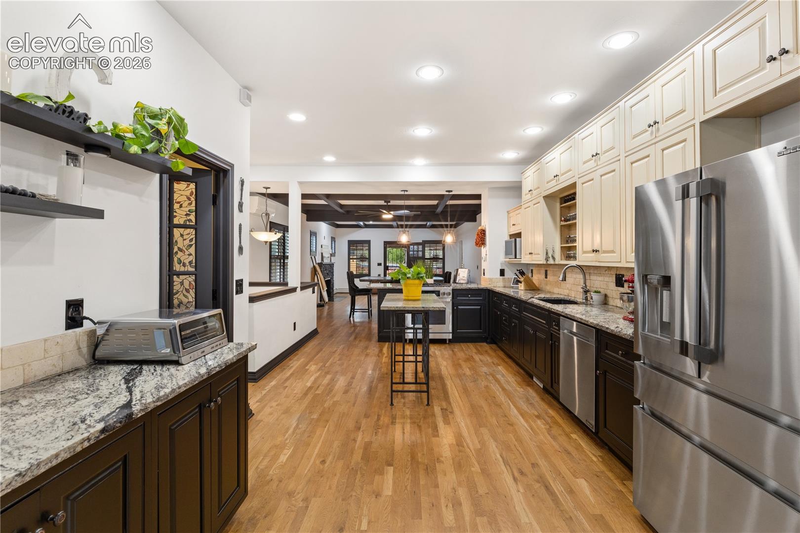Gourmet kitchen featuring wood-finish flooring, stainless steel appliances, granite countertops, and two-tone cabinetry with upper cream-colored and lower dark-stained cabinets