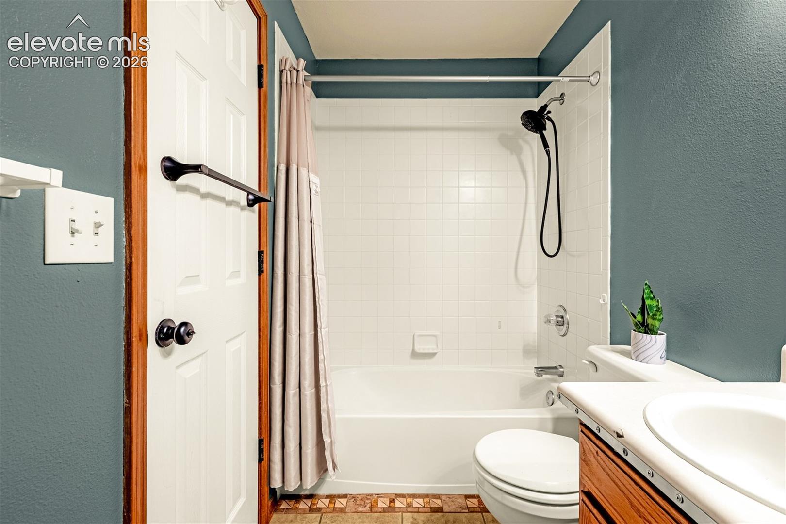 Bathroom featuring a white bathtub and shower combination with a black shower head, white tiled walls, a wood-finish vanity with a white countertop and sink, and green wall paint
