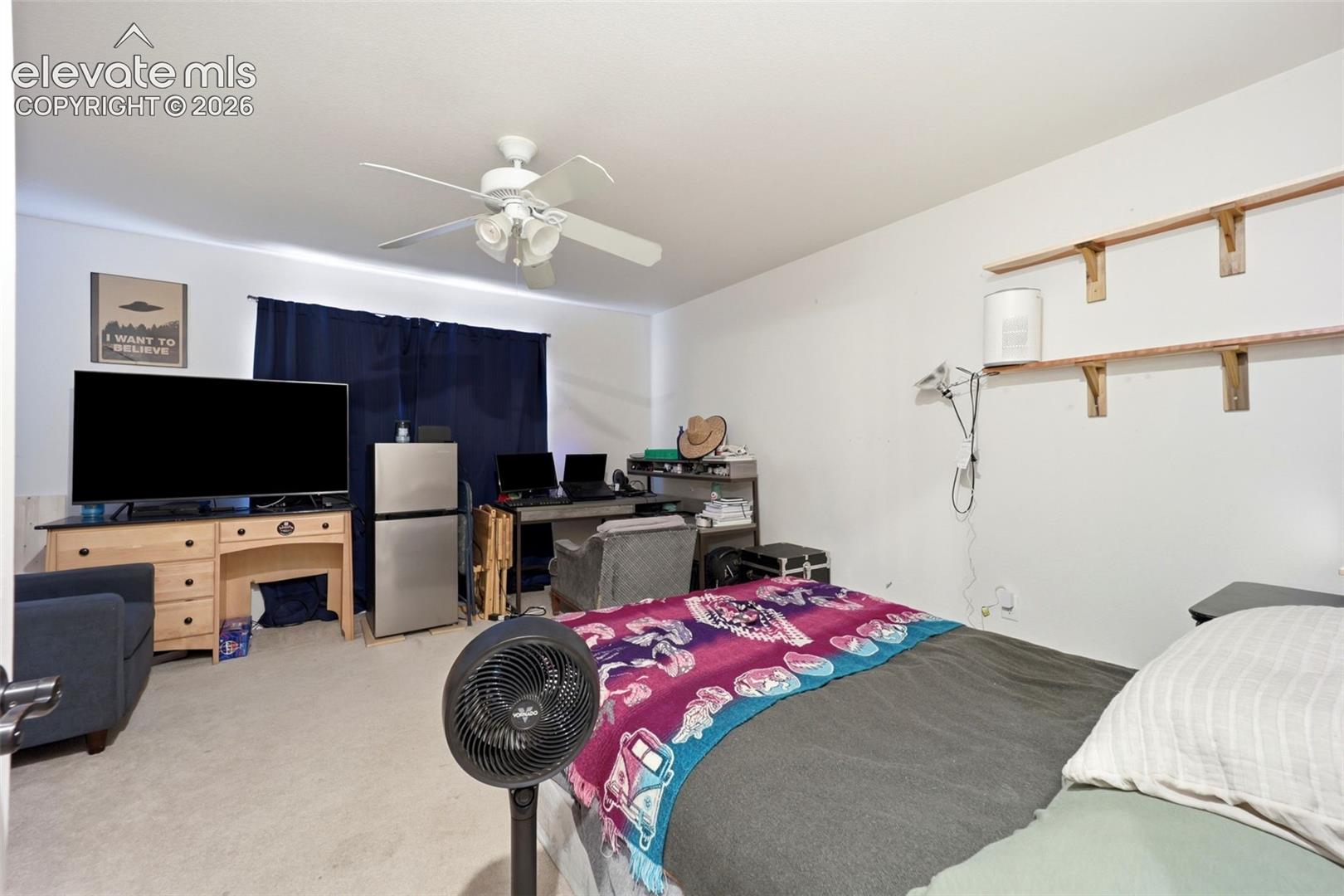Carpeted room with a ceiling fan, window with dark drapes, and built-in shelving units