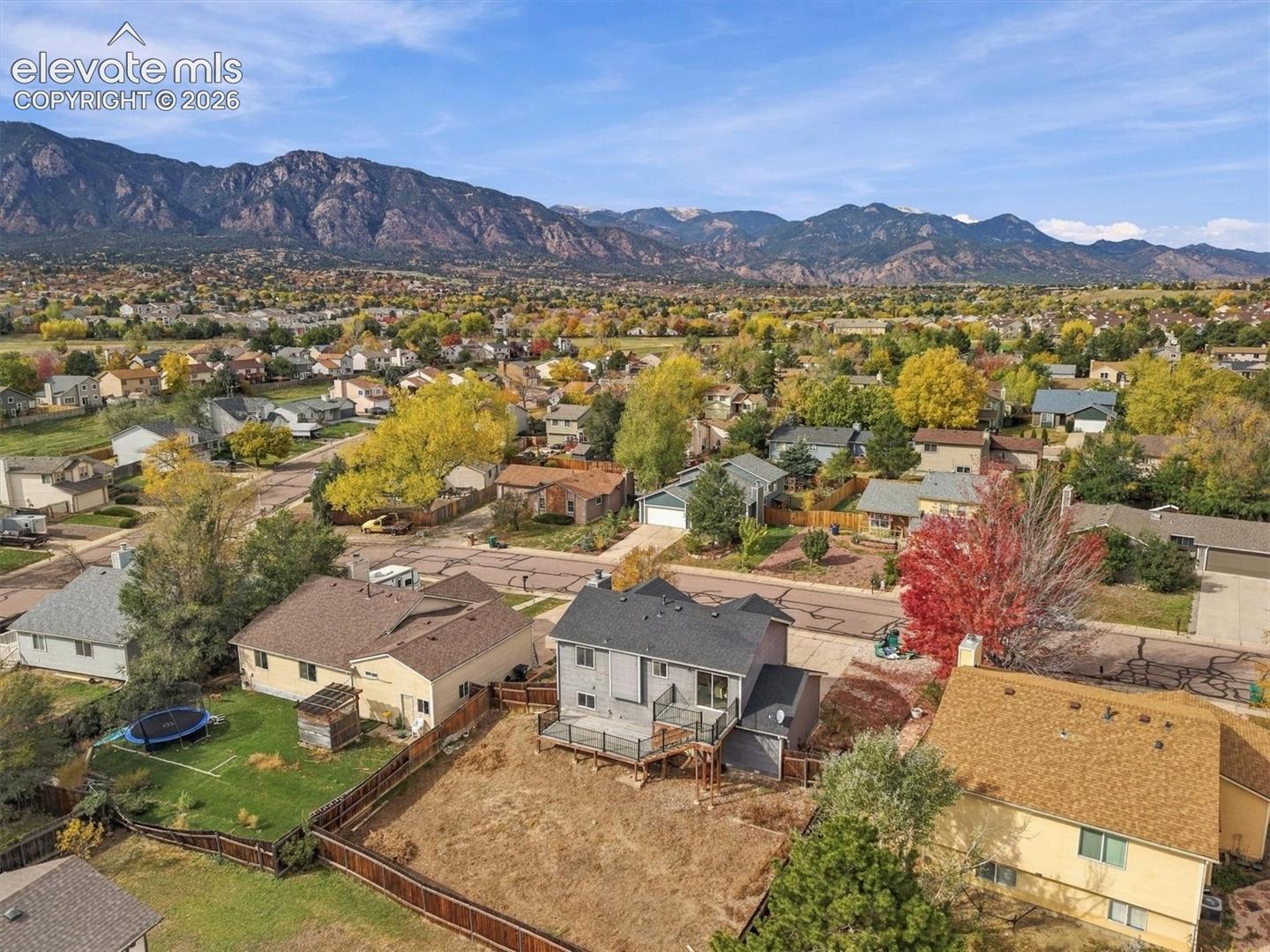 Aerial perspective showcasing a multi-level residence with a raised deck, fenced lot, and mountain backdrop