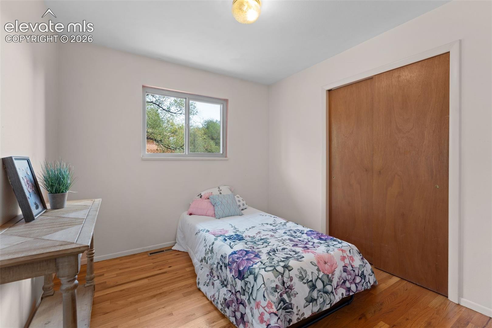 Hardwood flooring, natural light through a single window, white painted walls, and a built-in closet with wood-finish doors