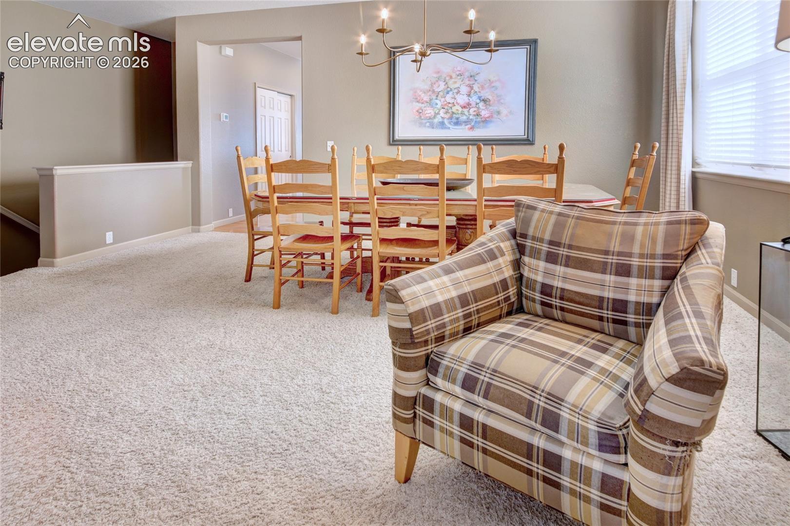 Carpeted flooring, multi-arm metal chandelier, and windows with neutral-toned window treatments