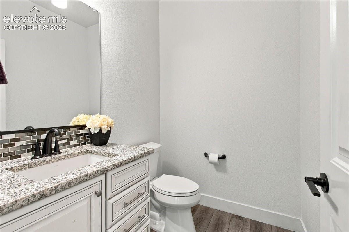 Bathroom featuring a white vanity cabinet with stone countertop, undermount sink, multi-tone glass tile backsplash, and matte black hardware