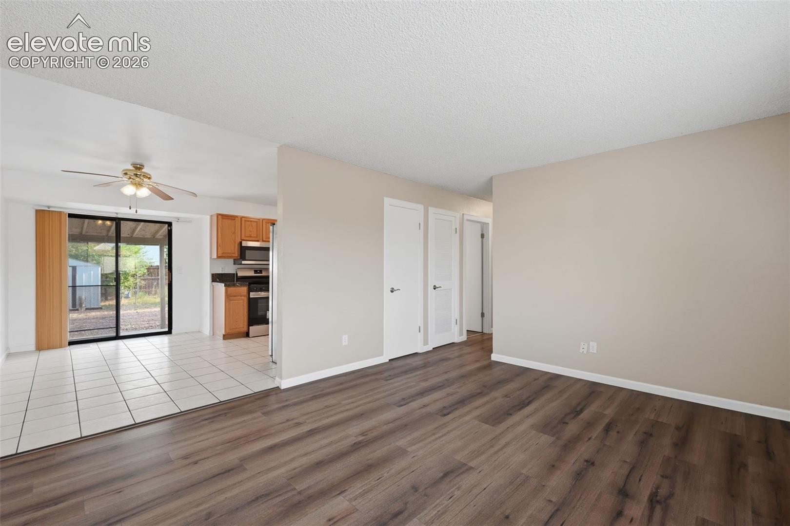Wood-finish flooring, white tile flooring, ceiling fan, sliding glass door, and recessed kitchen cabinetry