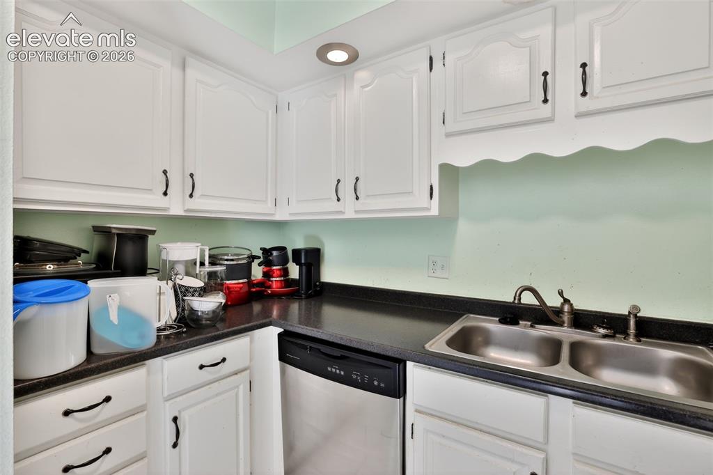 Kitchen featuring white cabinetry with dark hardware, dark countertops, a double-basin stainless steel sink, and a built-in dishwasher