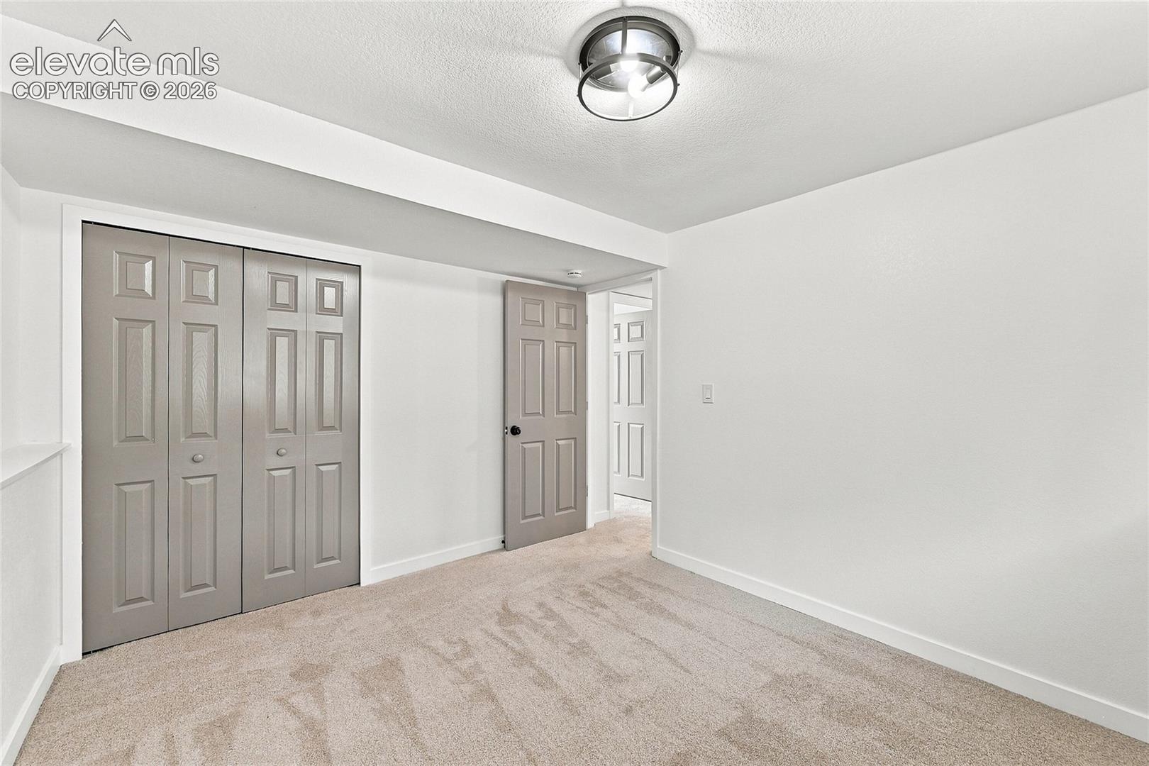 Neutral wall color, wall-to-wall carpeting, bi-fold panel doors, and a flush-mount ceiling light fixture