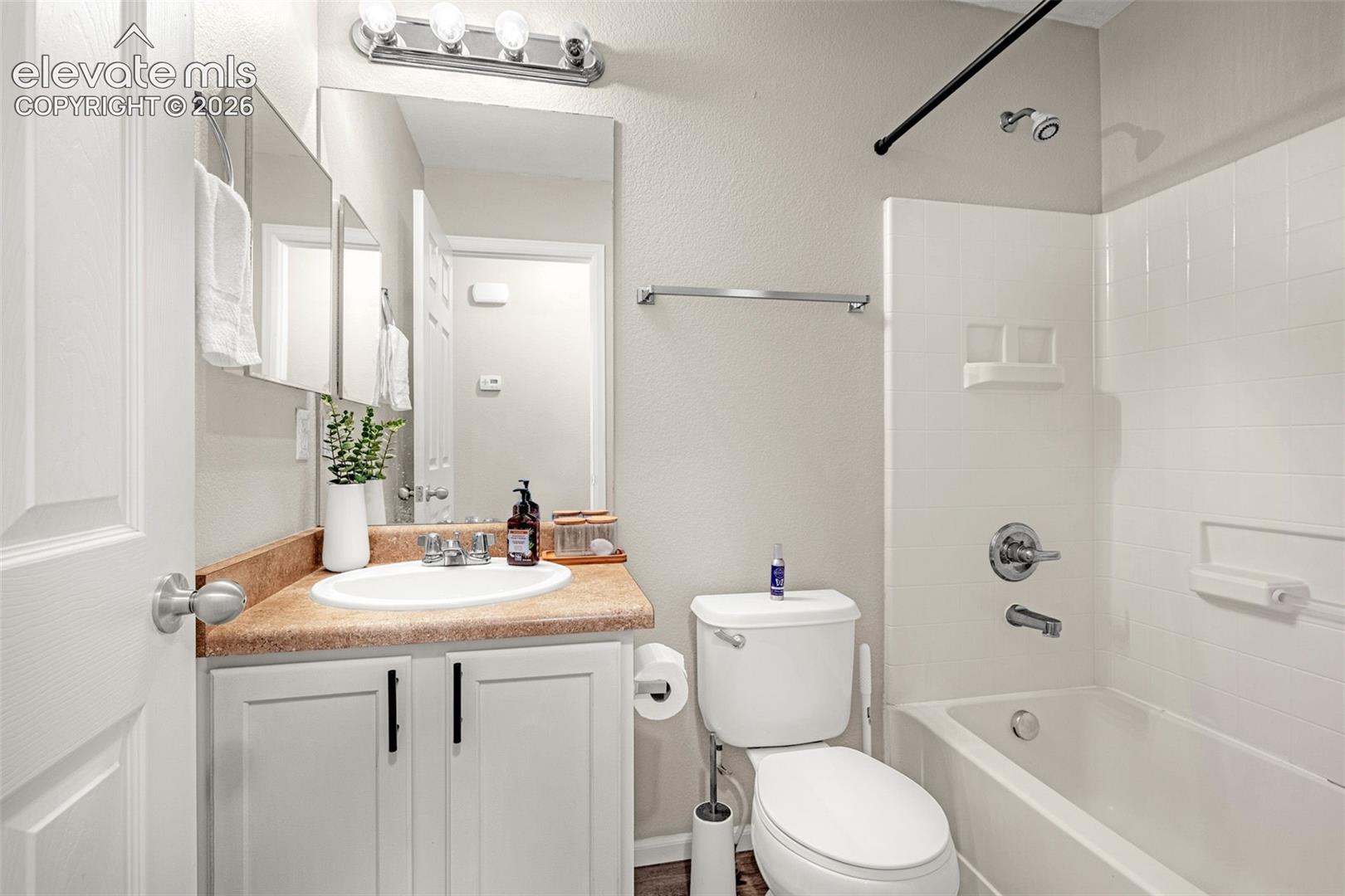 Bathroom featuring a vanity with a surface-mount sink, chrome faucet, white cabinetry with dark hardware, and a tub-shower combination with white subway tile surround