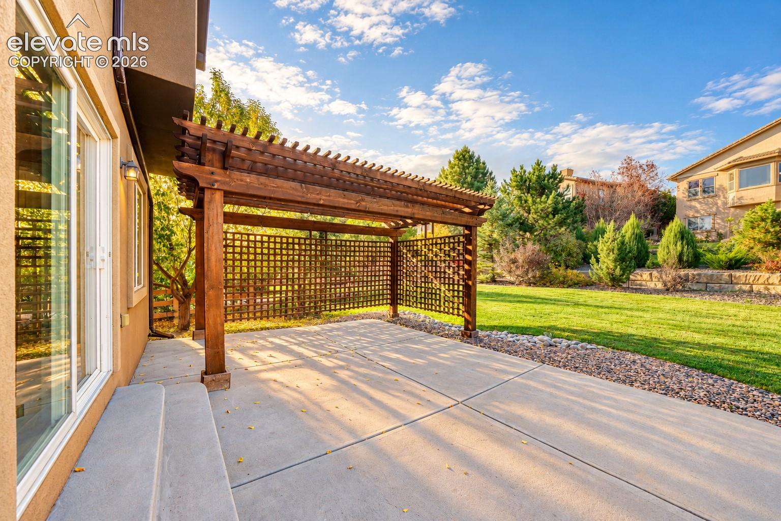 Expansive concrete patio with a wooden pergola, lattice privacy screen, and wide sliding glass door