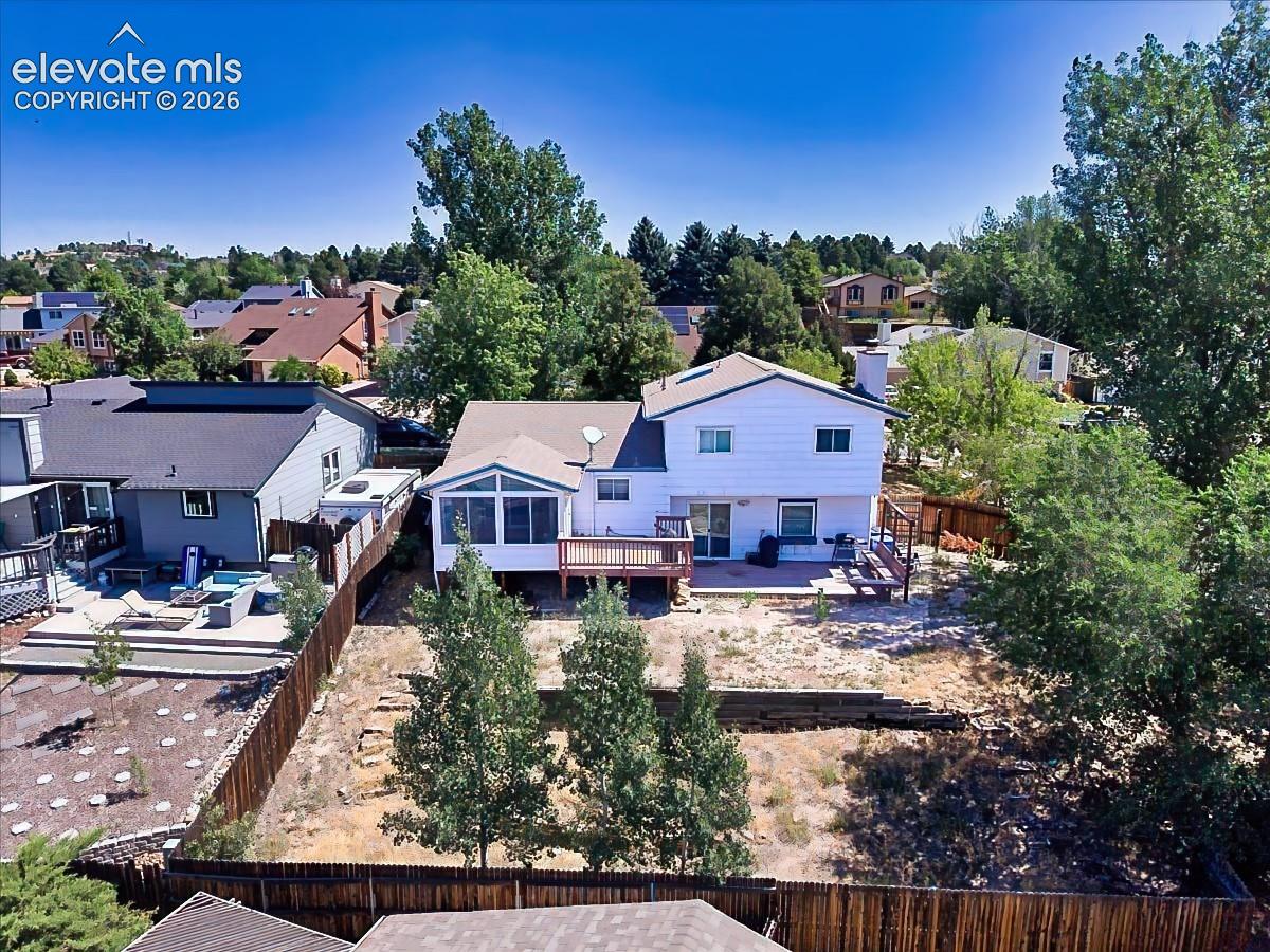Spacious fenced backyard featuring a large deck, enclosed sunroom, and mature trees that provide privacy and outdoor living potential.