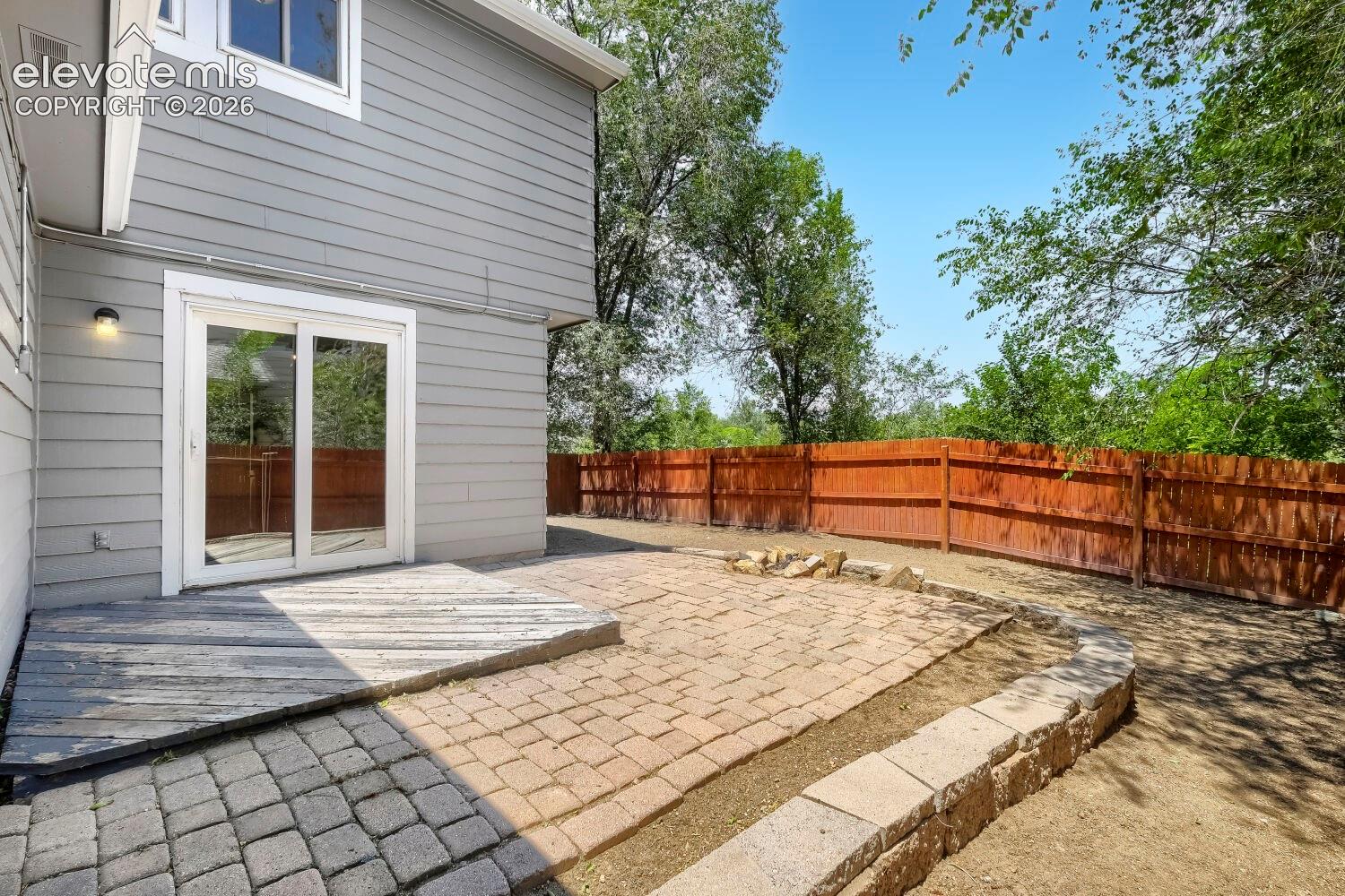 Private outdoor living space with sliding glass doors, a wood deck, a paver patio, stone block retaining walls, and a wood fence