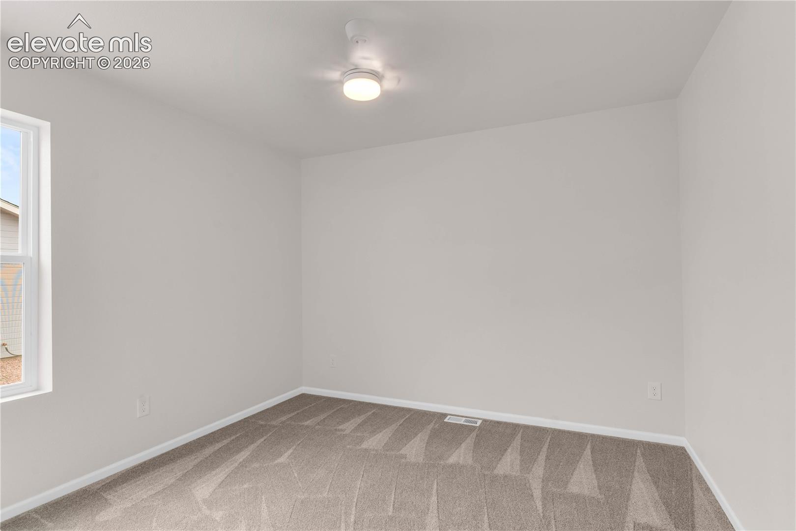 Neutral-toned interior space featuring wall-to-wall carpeting, a multi-pane window, and a central ceiling-mounted light fixture