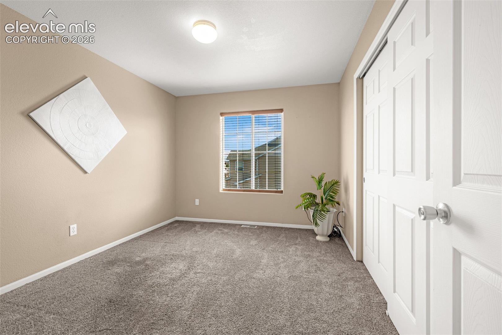 Neutral-toned walls, carpeted flooring, a window with wood-finish blinds, and a paneled sliding closet door