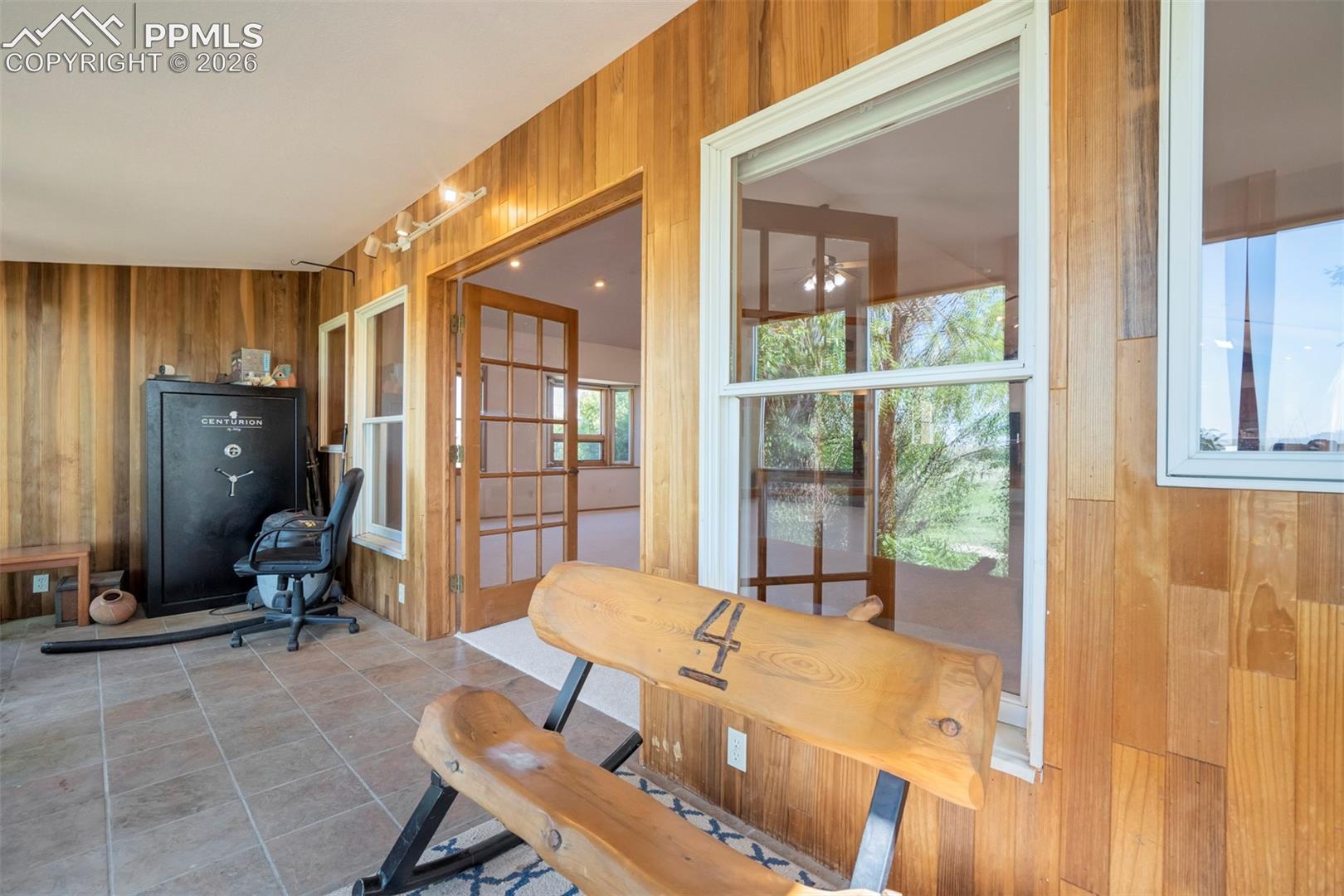Enclosed patio featuring extensive wood paneling, large white-framed windows, and neutral tile flooring