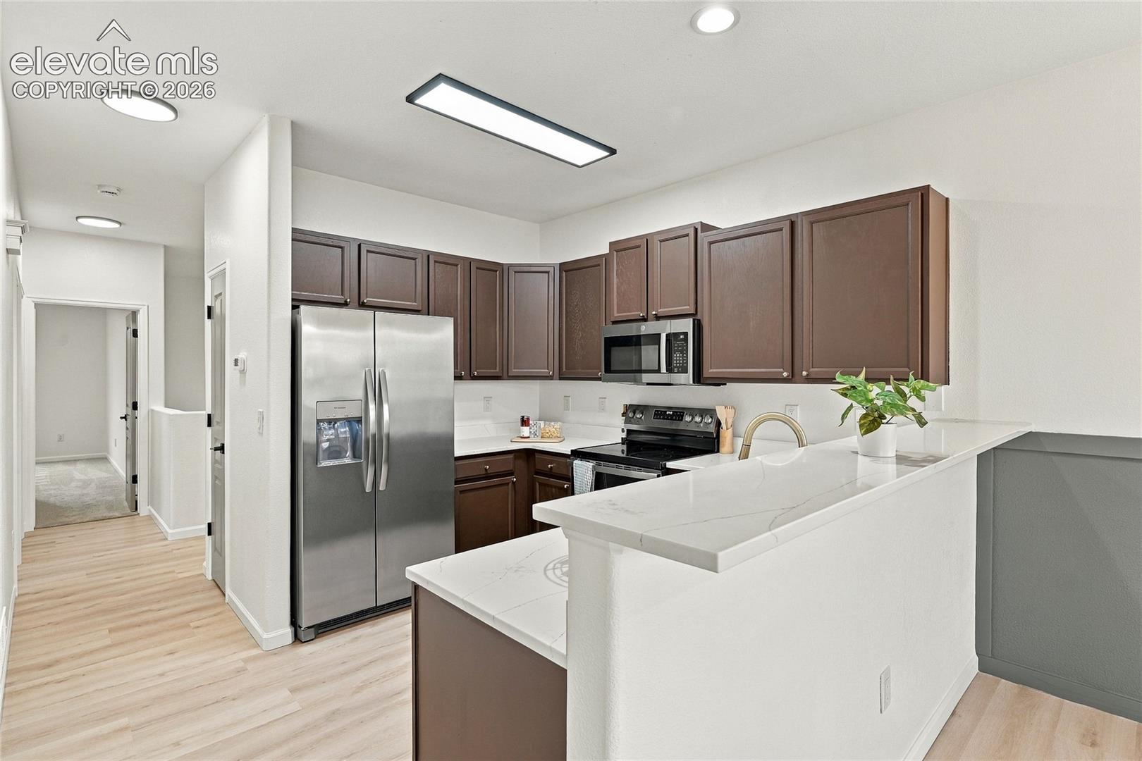 Kitchen featuring dark-toned cabinetry, quartz countertops with a breakfast bar, stainless steel appliances, recessed ceiling lighting, and wood-finish flooring