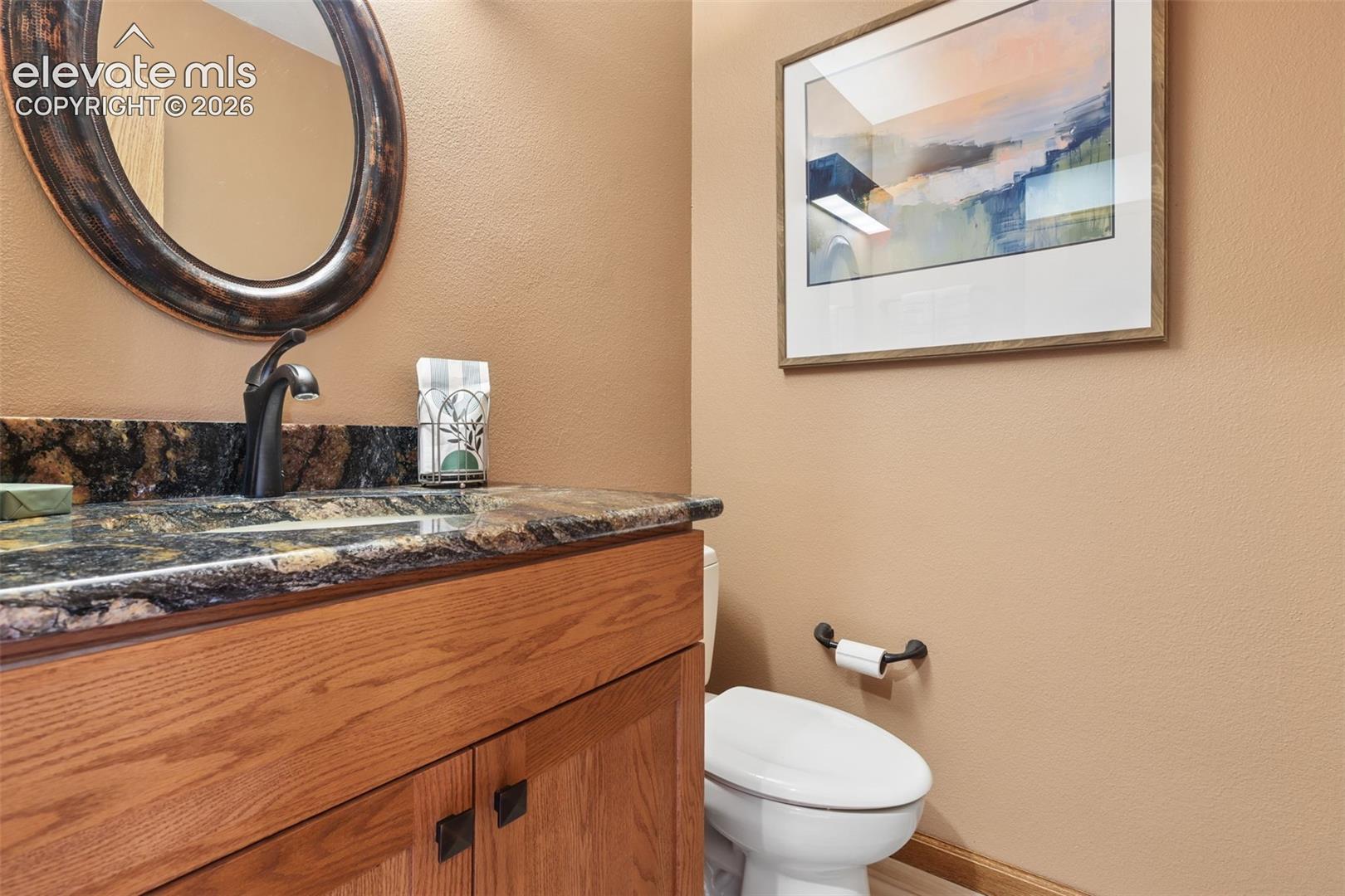1/2 bath off the kitchen with granite counters and decorative lighting.