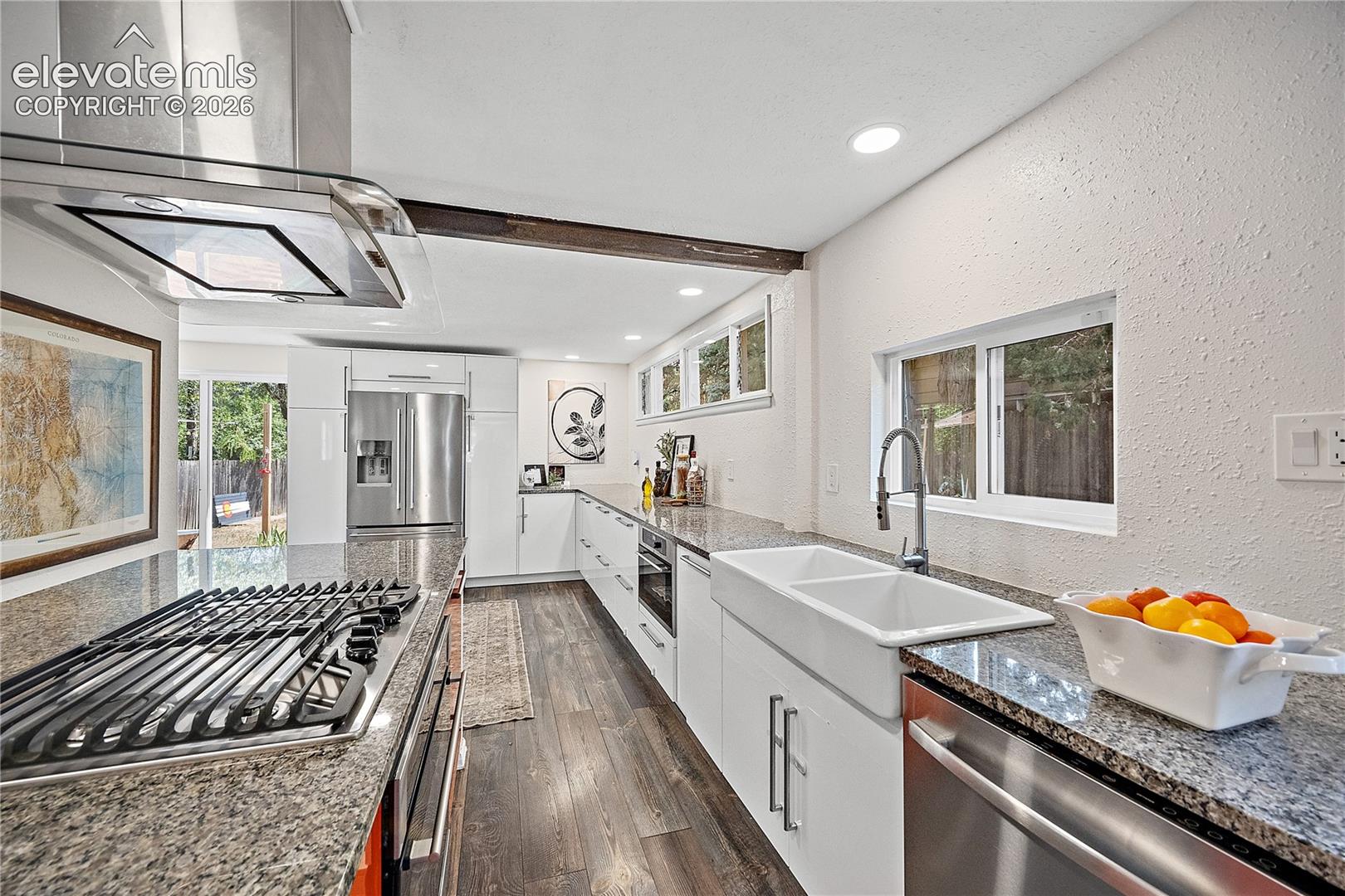 Modern kitchen featuring stainless steel appliances, granite countertops, white cabinetry, a double basin farmhouse sink, and wood-finish flooring