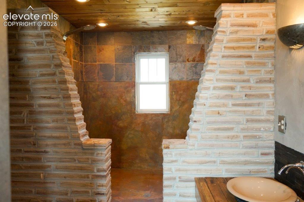 Stone-clad shower enclosure featuring a fixed window and a wood-finish ceiling with recessed lighting
