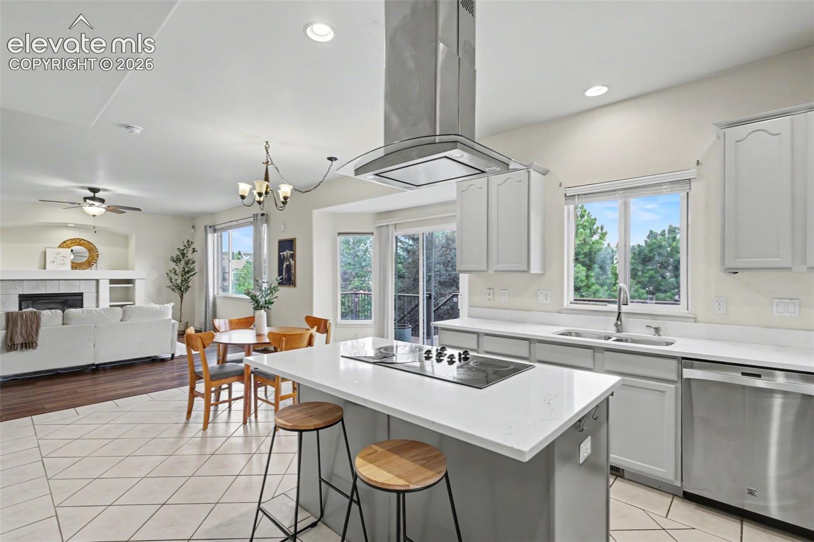 Modern kitchen featuring an island cooktop with overhead range hood, light cabinetry, stainless steel appliances, and a dual basin sink