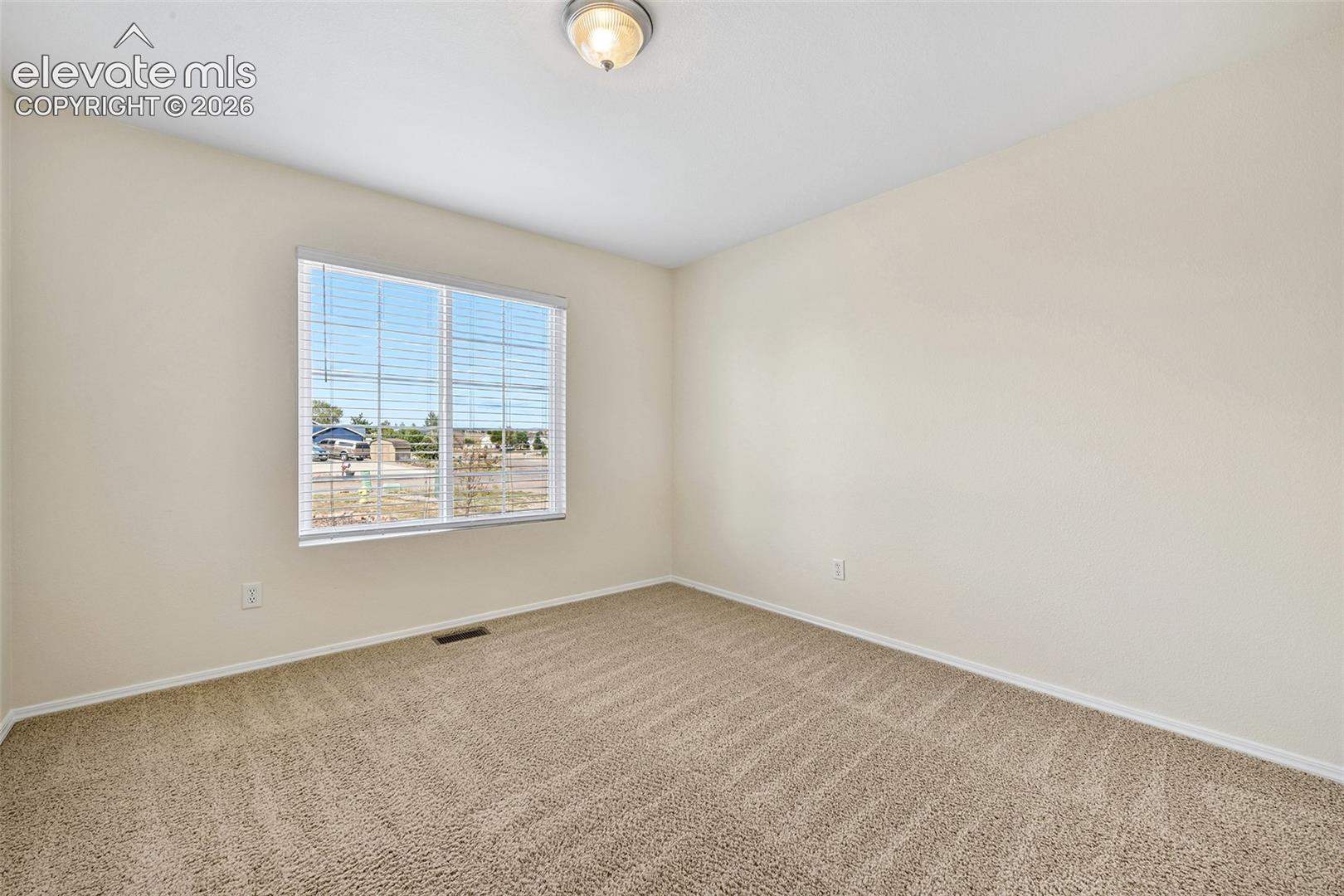 Neutral tone wall paint, textured carpeting, window with horizontal blinds, and a flush mount ceiling light fixture