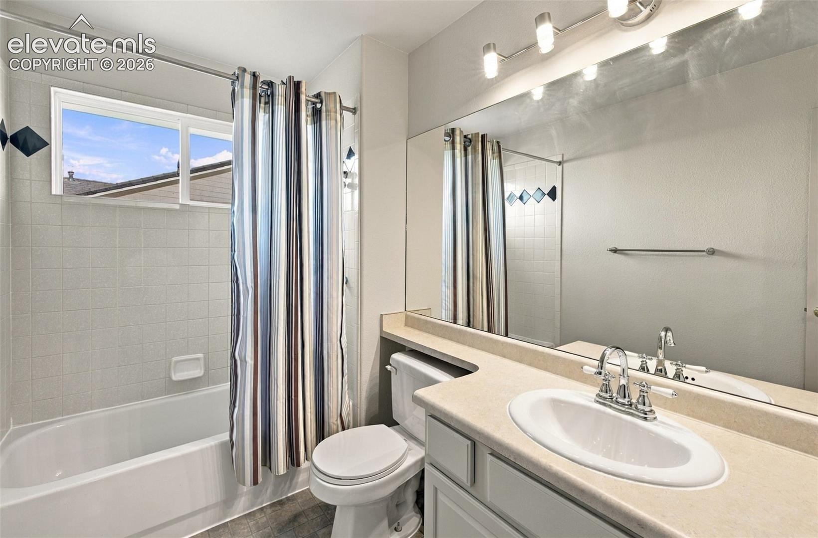 Full-width vanity with integrated countertop and sink, large wall-mounted mirror, multi-bulb vanity lighting, and a bathtub with tile surround