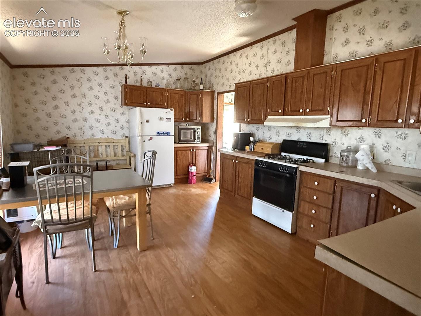 Kitchen featuring wooden cabinetry, laminate countertops, a gas range, a multi-light chandelier, and wood-finish flooring