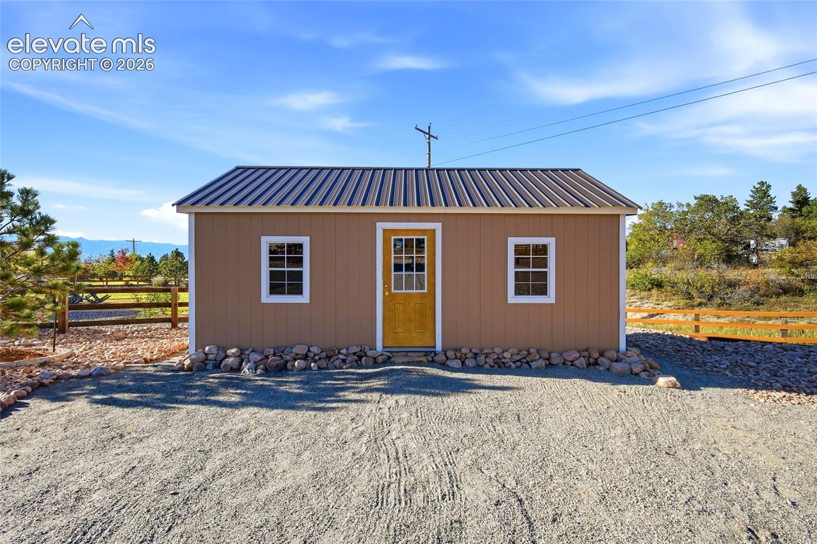 Detached structure featuring a metal roof, paneled siding, dual double-hung windows, and rock perimeter landscaping