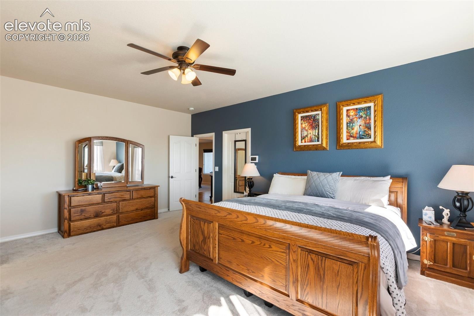 Spacious room featuring a navy blue accent wall, neutral carpeting, and a multi-blade ceiling fan with integrated lighting